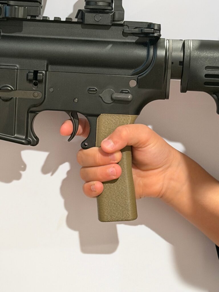 A young shooter's hand fully wrapped around the FDE Rokin Youth AR Pattern Grip, with the trigger finger resting on the face of the trigger